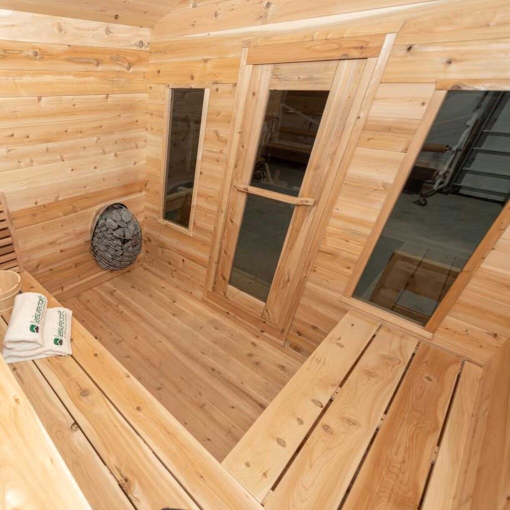 Indoor view of the Georgian cedar sauna showing benches, glass door, and heater stones in a compact cabin layout for outdoor wellness.